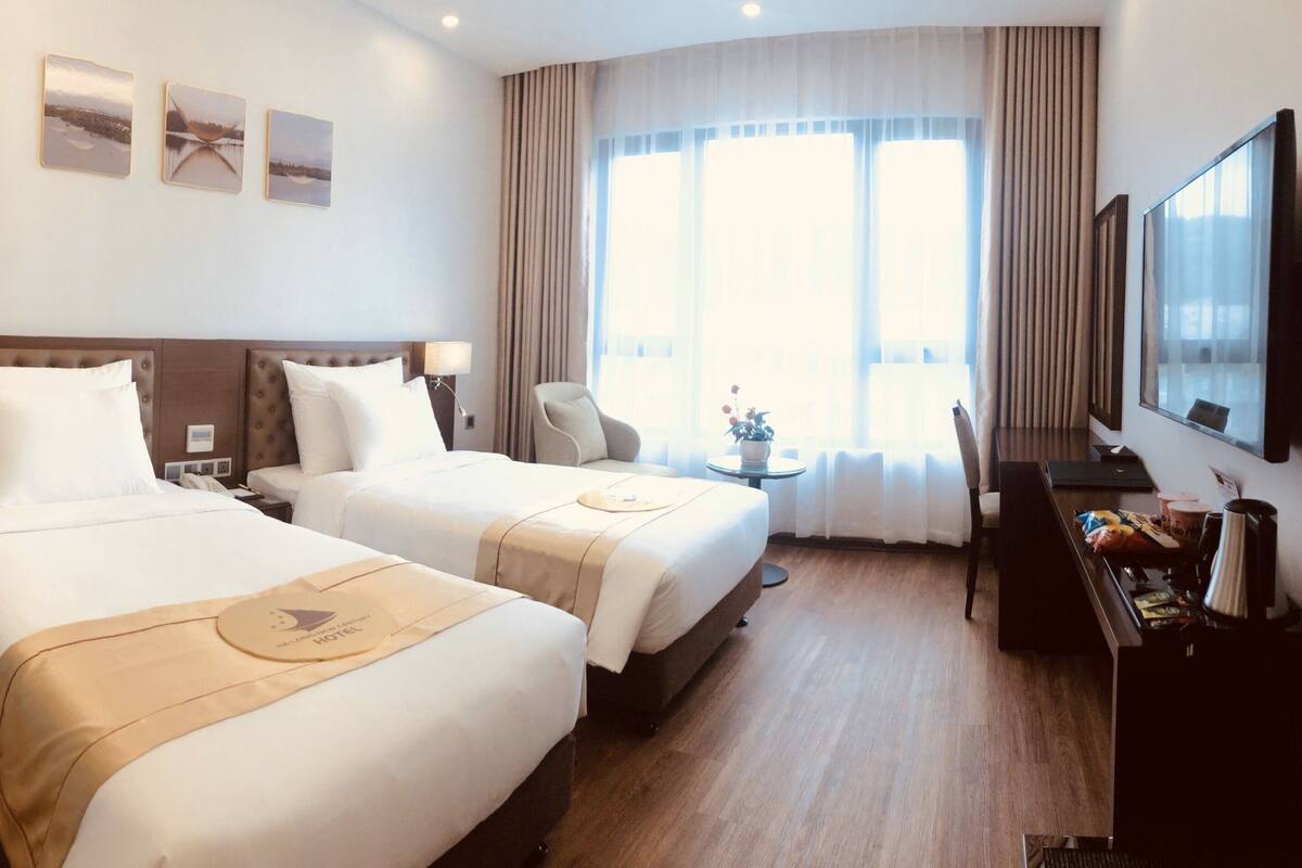 Een hotelkamer met twee bedden, een bureau, een stoel, een televisie en een raam met gordijnen.