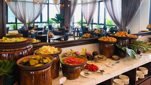 A buffet with various dishes in large ceramic pots, a marble counter, and a view of the dining area through large windows with curtains. - Ha Long New Century Hotel (Bai Chay)