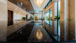 A spacious hotel lobby with a reflective floor, a central chandelier, and large windows offering views of the outdoors. - Ha Long New Century Hotel (Bai Chay)