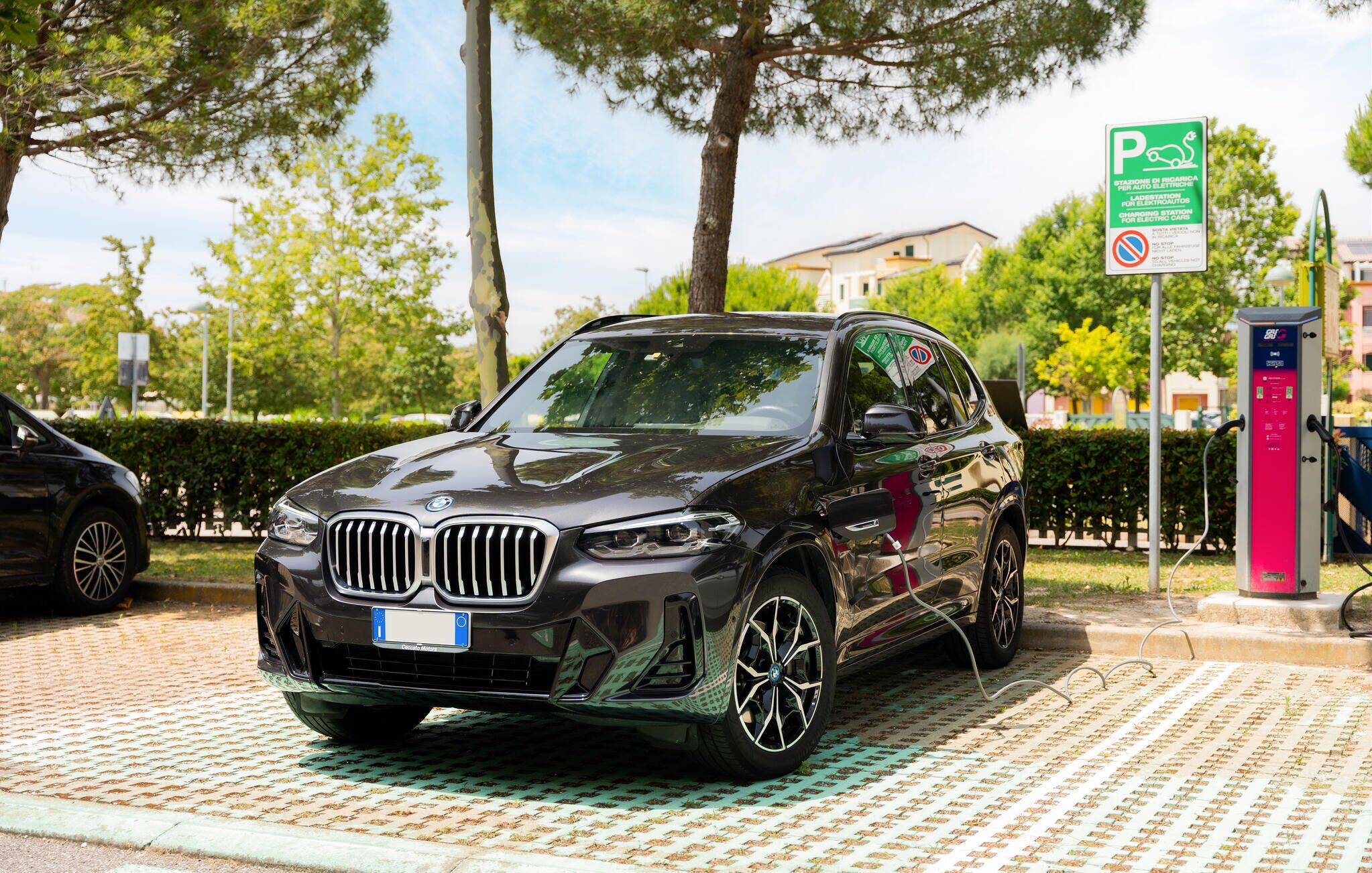 A black BMW SUV parked at a charging station with a green sign indicating it is a public charging station.