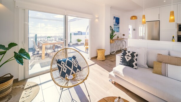 Ein modernes Wohnzimmer mit einem weißen Sofa, einem Korbstuhl und einem Essbereich mit Tisch und Stühlen.