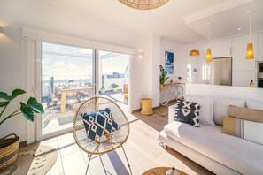 Un salon moderne avec un canapé blanc, un fauteuil en osier et un coin repas comprenant une table et des chaises.