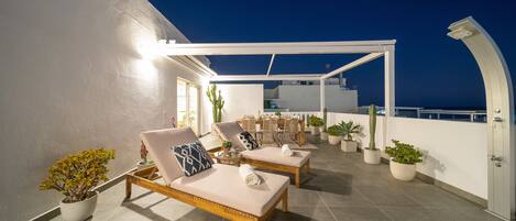Una terraza en la azotea con dos sillones, una zona de comedor y plantas en macetas.