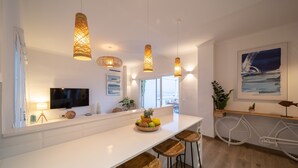 Eine moderne Küche mit weißer Arbeitsplatte, Holzbarhocker, hängenden Pendelleuchten, einem großen Fenster und einem an der Wand befestigten Fahrrad.