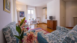 Una sala de estar con sofás de estampado floral, una mesa de comedor con sillas, un televisor sobre un mueble de madera y una ventana con cortinas.