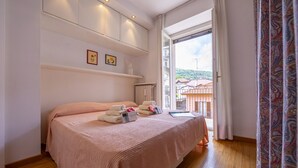 Un dormitorio con cama, radiador, ventana y vistas a edificios.