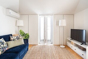 Una sala de estar moderna con un sofá azul, un televisor de pantalla plana y un ventanal grande.