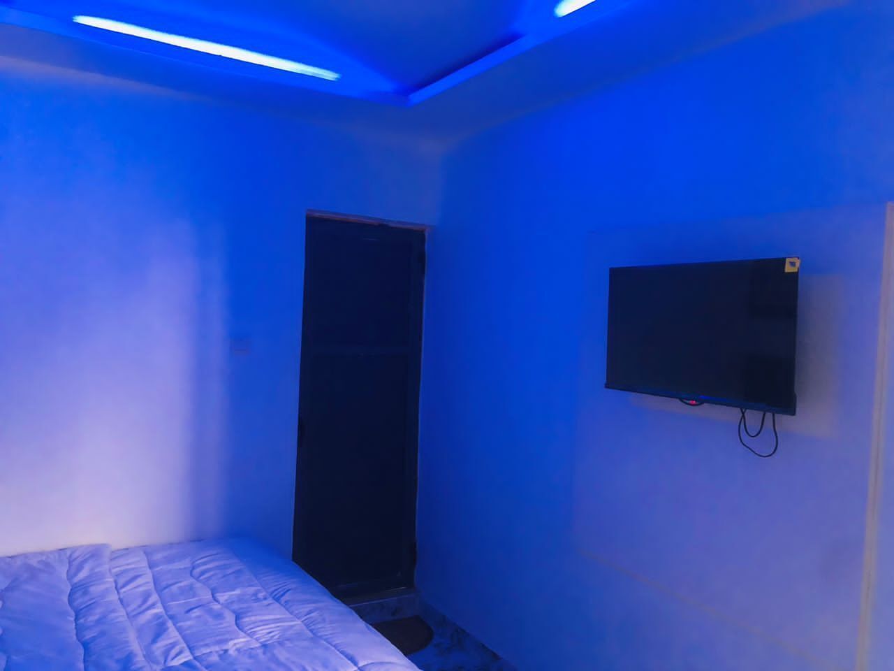 Un dormitorio con una cama, un televisor en la pared y una puerta.