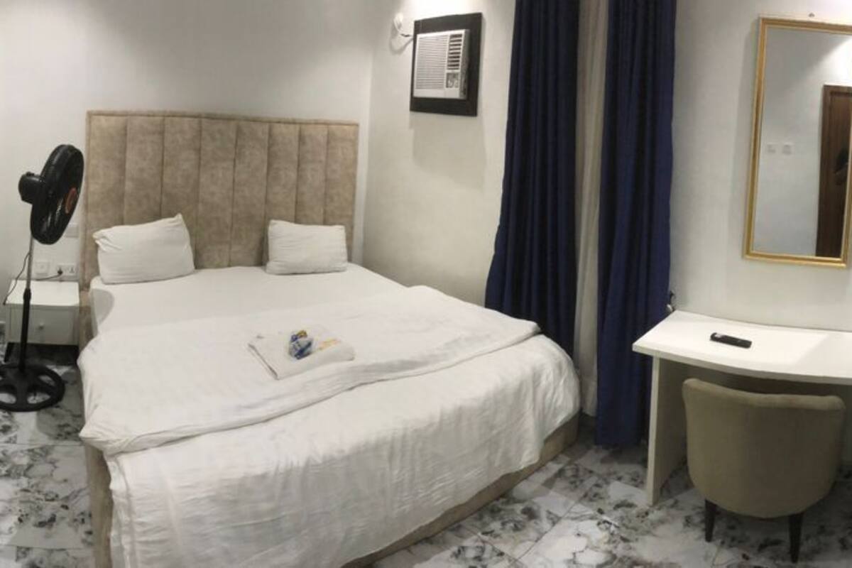 A hotel room with a bed, bedside table, desk, chair, and a TV on the wall.
