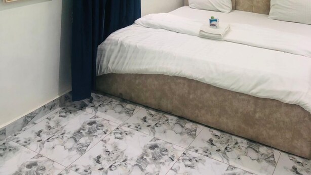 Ein Schlafzimmer mit Bett, Kopfstück, Vorhang, gerahmtem Bild und Fliesenboden.