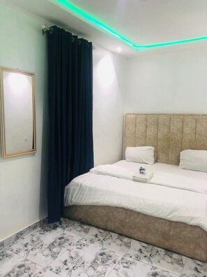 A bedroom with a bed, a headboard, a curtain, a framed picture, and a tiled floor. - LAQUINTA Hotel by Juicebox (Lagos)