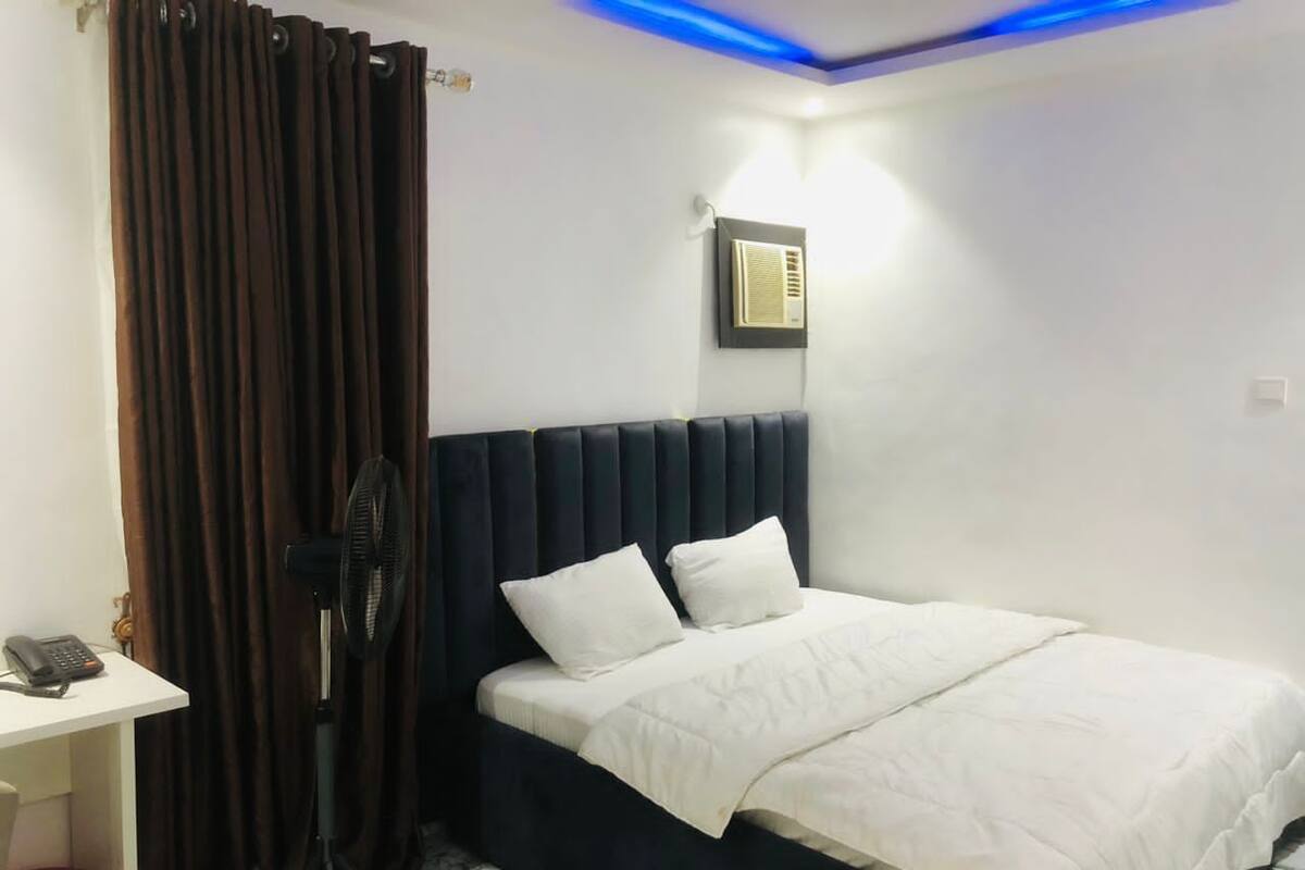 A bedroom with a bed, a desk, a fan, and a curtain.
