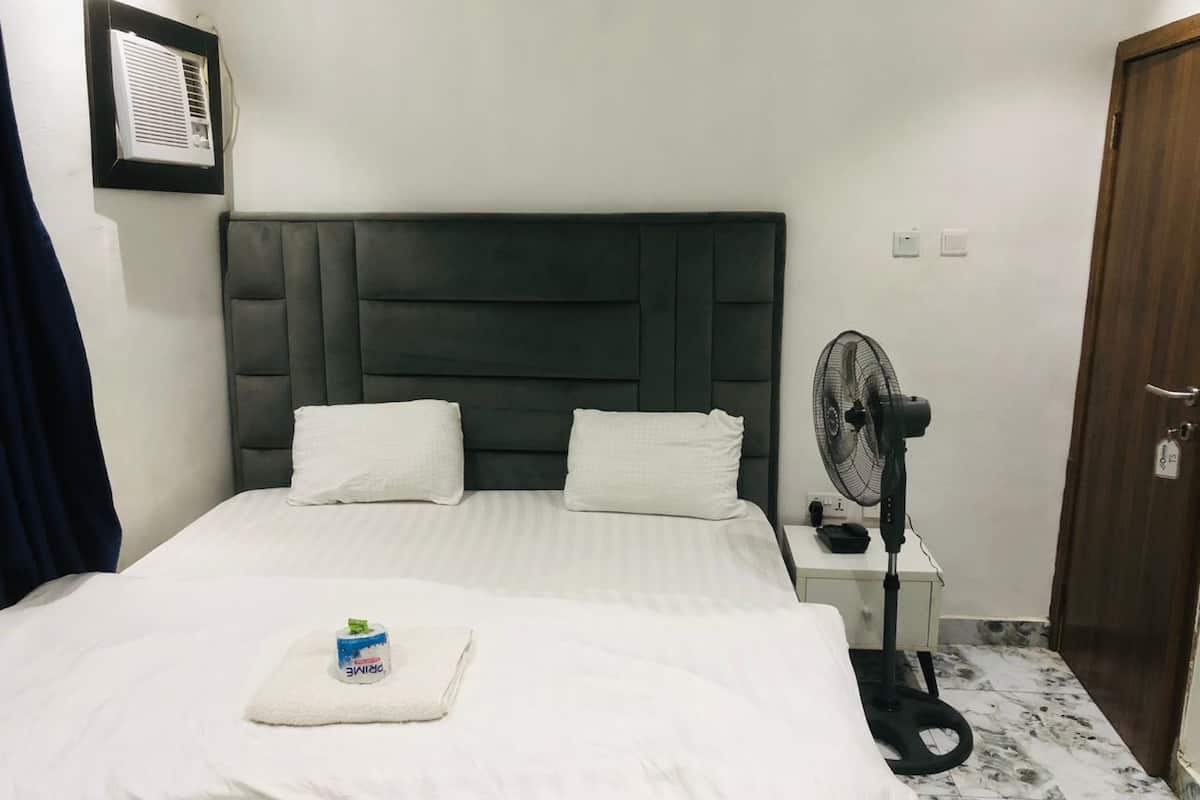 A neatly made bed with white linens, a bedside table with a fan, and a small item on the bed.