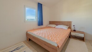 Ein Schlafzimmer mit einem hölzernen Bett, einem Nachttisch, einer Lampe, einem Fenster mit blauen Vorhängen und Blick auf die Berge.