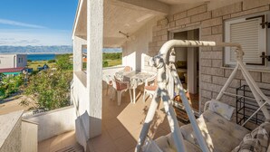 Ein Balkon mit Tisch und Stühlen, Blick auf das Meer und ein Gebäude mit schrägem Dach.