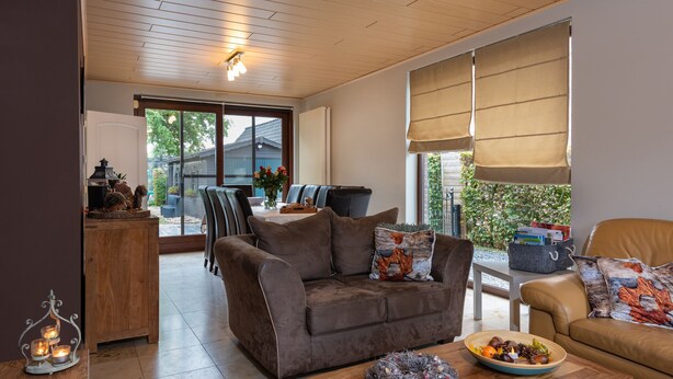 Ein gemütliches Wohnzimmer mit einer braunen Couch, einem Holztisch und einem Essbereich im Hintergrund.