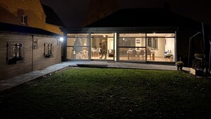 Ein modernes Haus mit Glasfassade, einem Weihnachtsbaum und einem Essbereich, der durch die Fenster sichtbar ist.