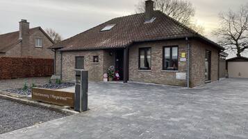 A small brick building with a tiled roof, a sign indicating 'Vacantewoning t Reigersnest', and a paved driveway.