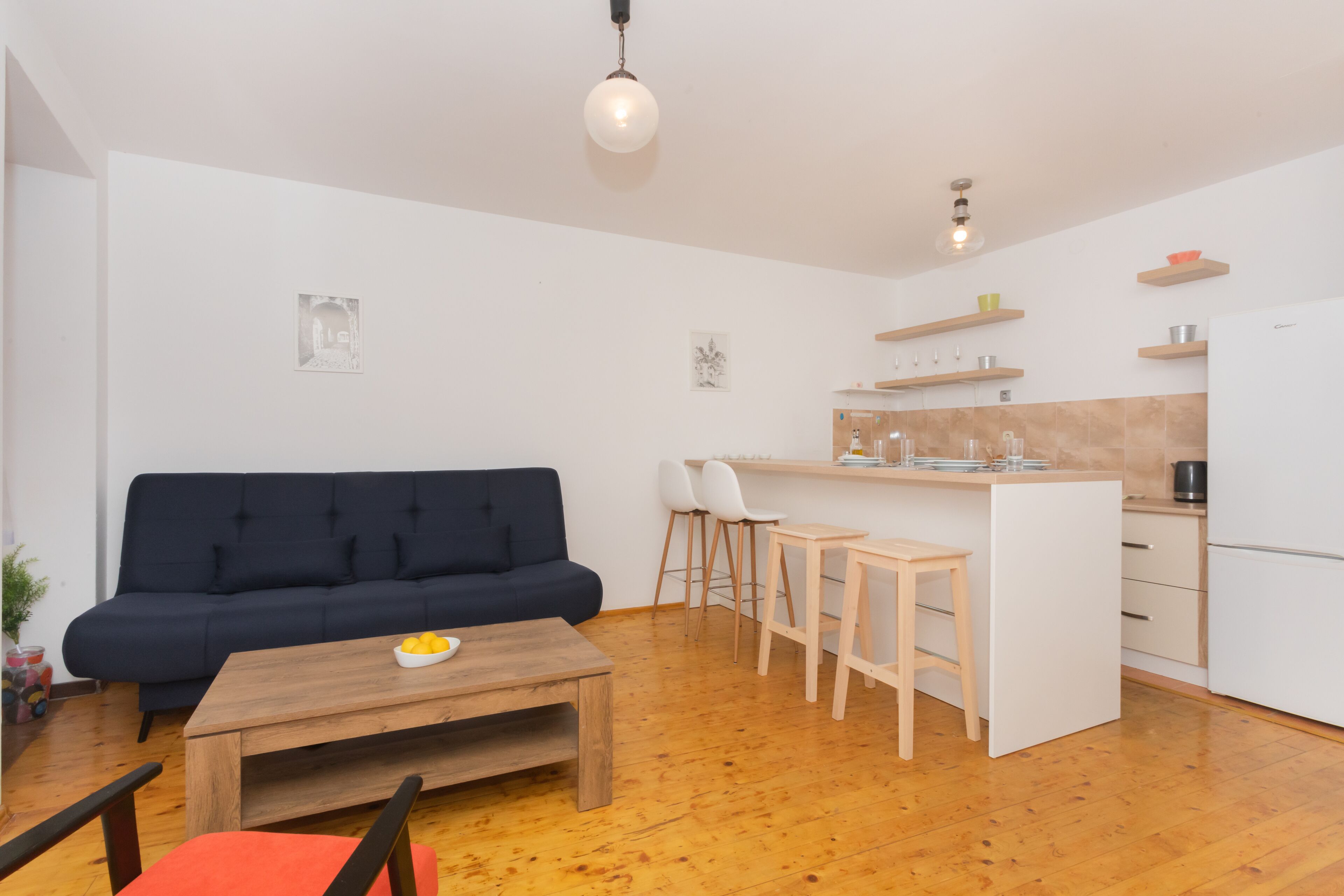 A modern living space with a sofa, a coffee table, and a kitchen area with stools and a countertop.