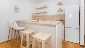 Eine moderne Küche mit einer zentralen Kochinsel, zwei weißen Barhocker, einem weißen Kühlschrank und Holzregalen über der Arbeitsfläche.