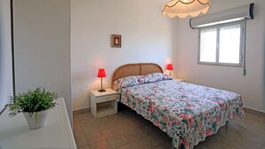 A bedroom with a bed, two bedside tables, a hanging lamp, a window, and a potted plant. - app.to Scirocco (Ragusa)