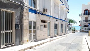 A narrow urban street lined with buildings, some with balconies and others with ground-level shops. - app.to Scirocco (Ragusa)