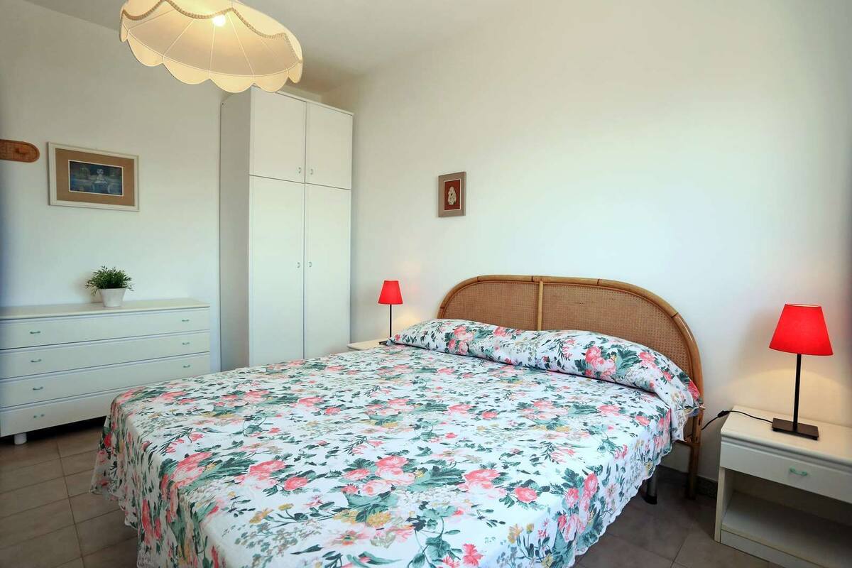 Un dormitorio con cama, mesita de noche, cómoda, armario y dos lámparas de pared.