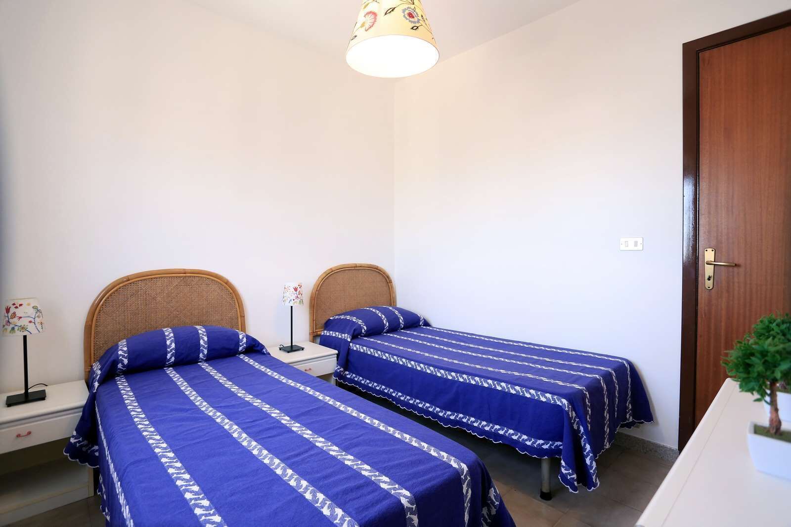 Ein Schlafzimmer mit zwei Einzelbetten, einem Nachttisch mit Lampe und einer Holztür.