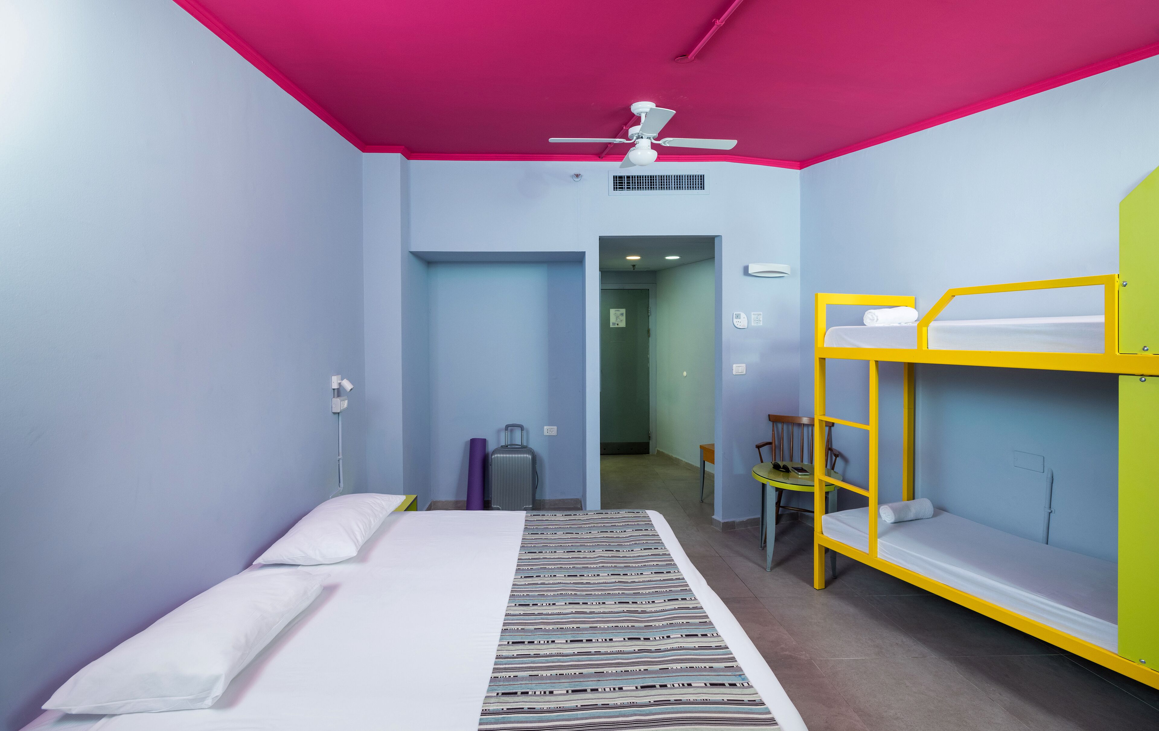 Una habitación con una cama, una litera, una maleta y una silla.