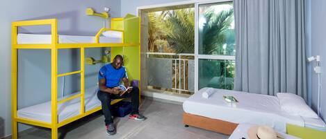 A room with bunk beds, a bed, a window with a view of palm trees, and a curtain.
