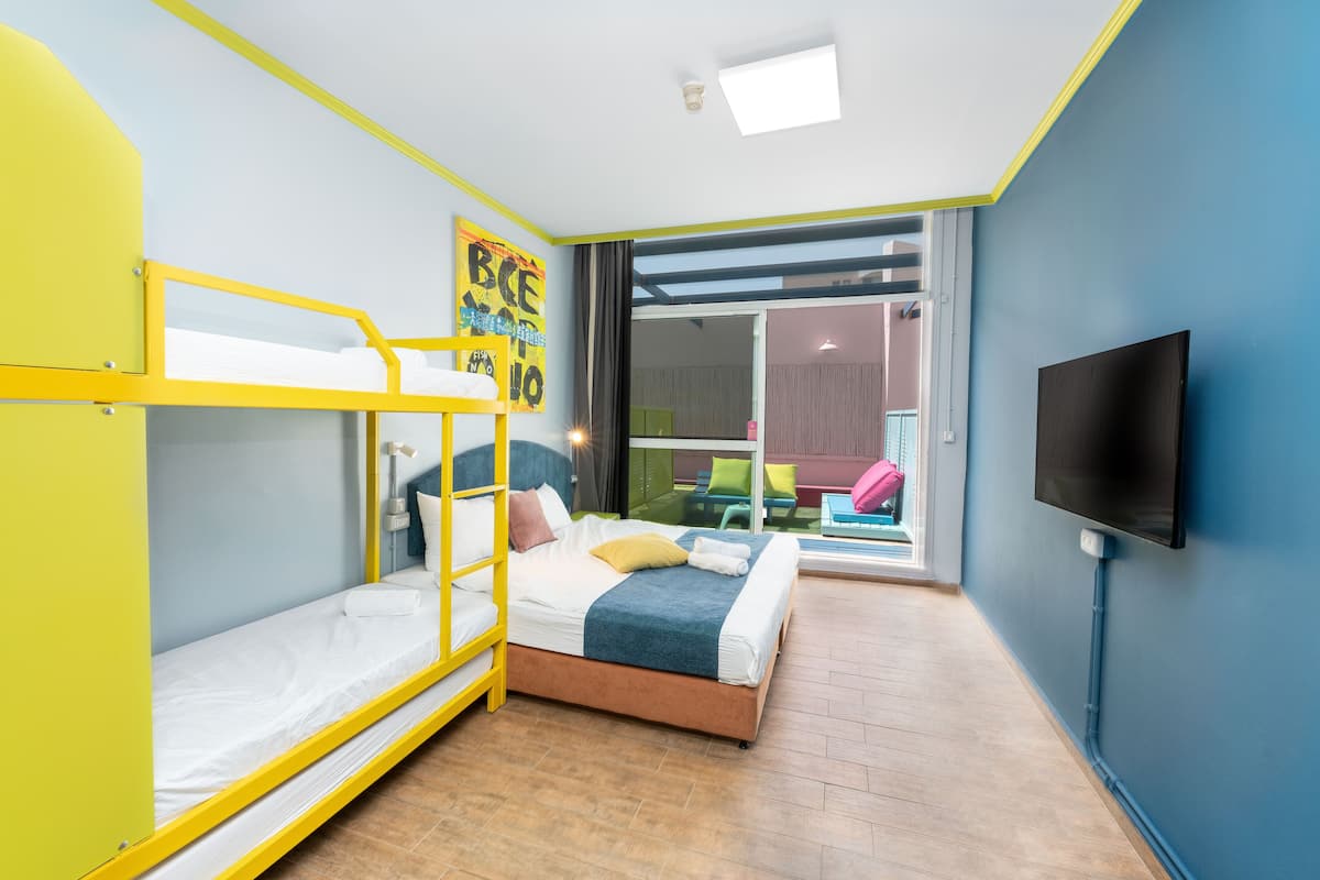 A room with a bunk bed, a single bed, a TV, and a view of an outdoor area.