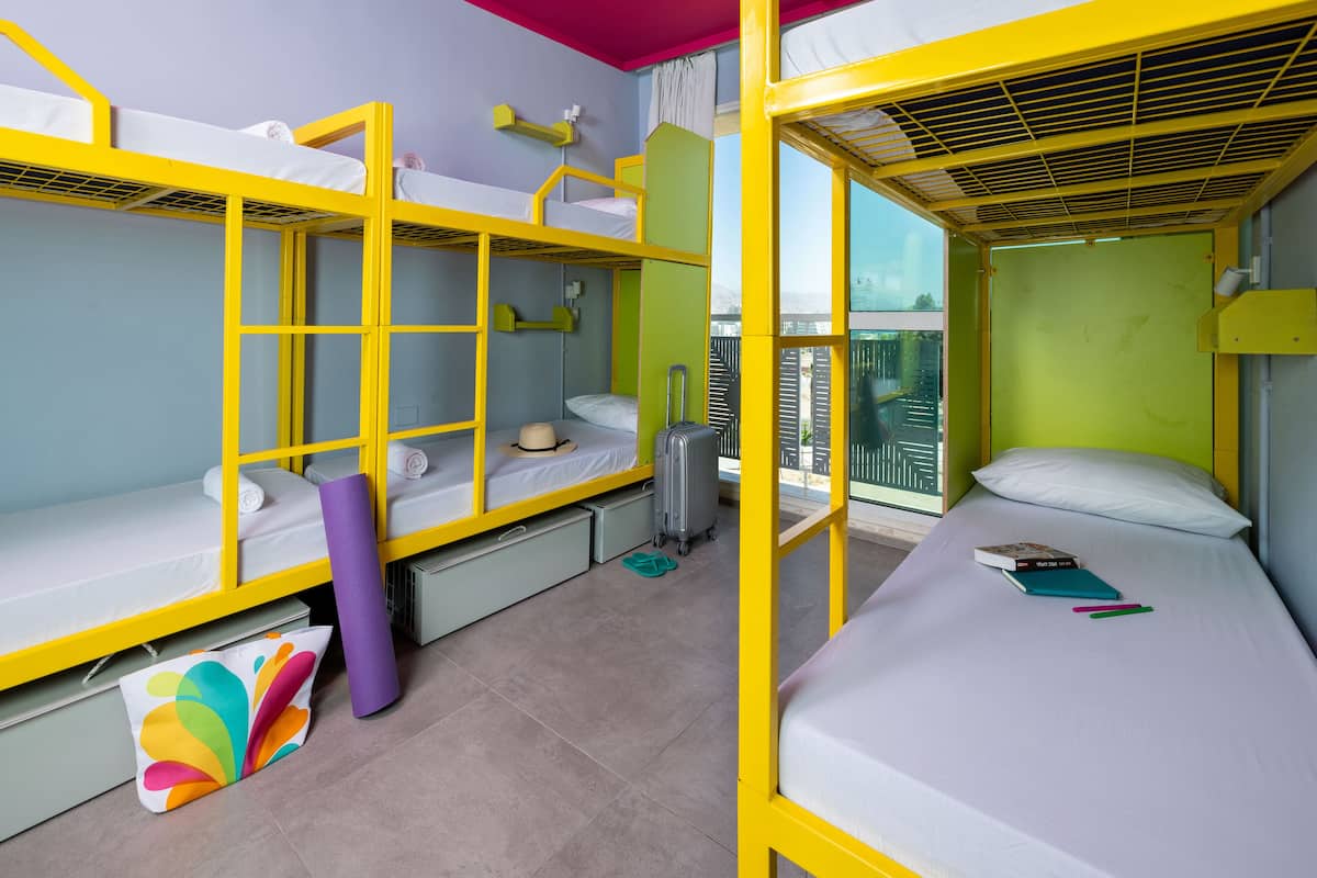 A dormitory-style room with bunk beds, a suitcase, a yoga mat, and a book on the bed.