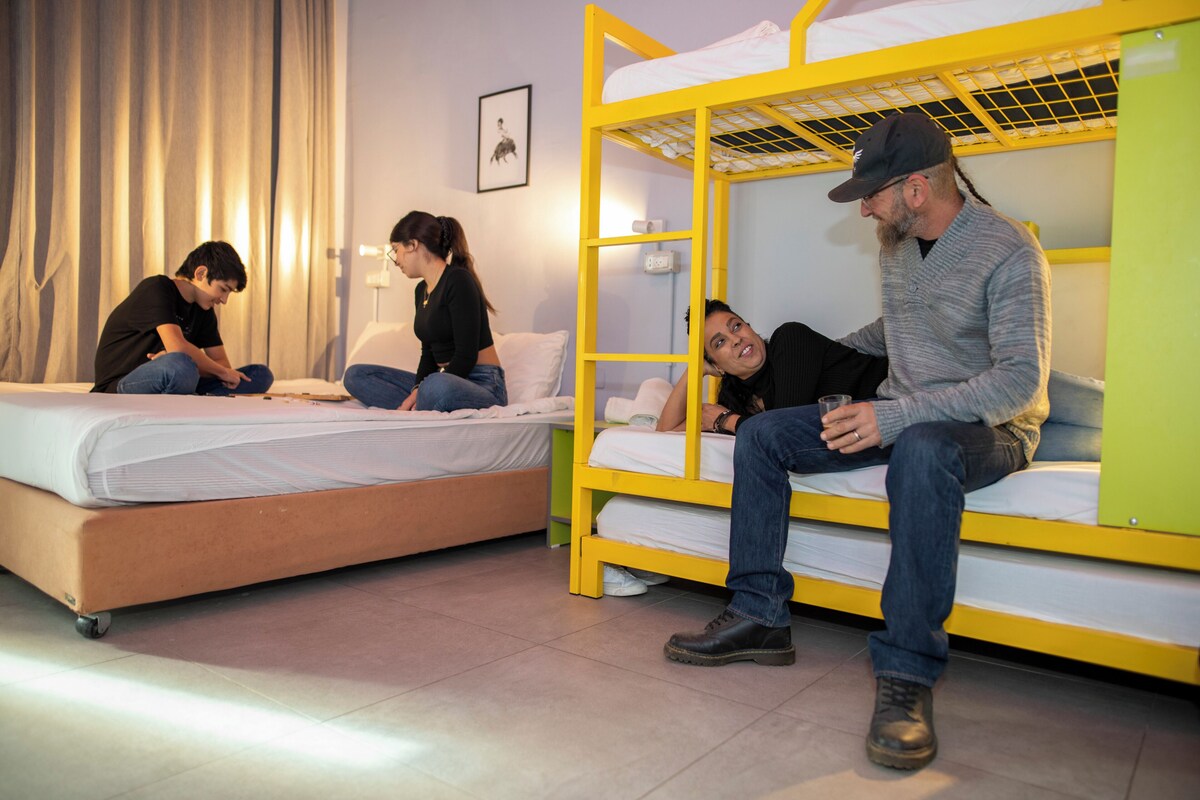 A dormitory room with bunk beds, a bed, and a window with curtains.