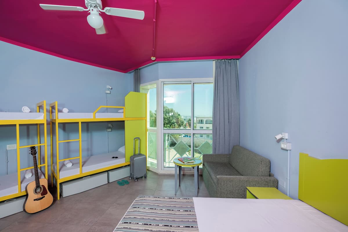 A room with bunk beds, a sofa, a table, a guitar, and a view of the outdoors.