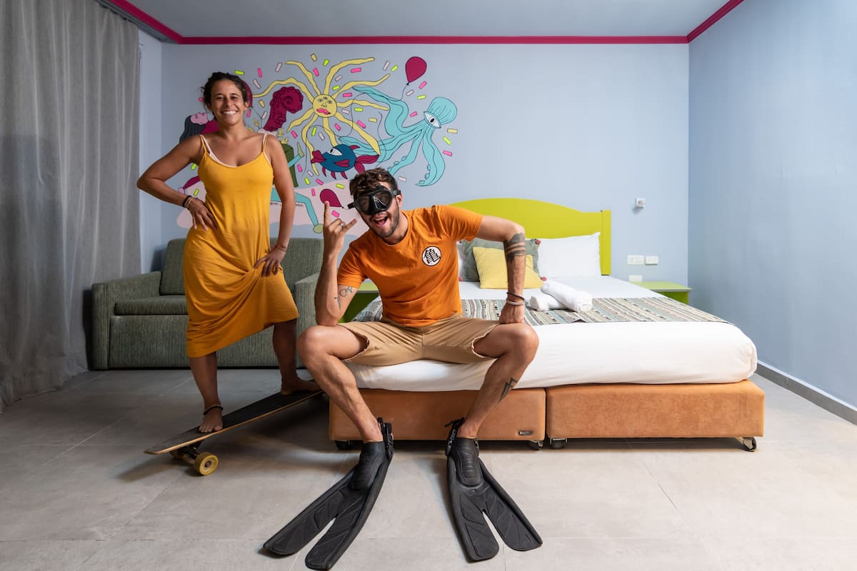 A room with a bed, a sofa, and a colorful mural on the wall.