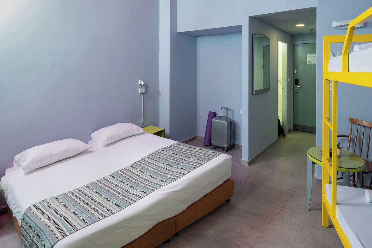 A bedroom with a bed, a bunk bed, a suitcase, a chair, and a table.