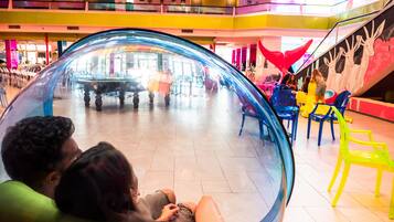 Una gran esfera transparente en un espacio público, con piso de baldosas y sillas de colores alrededor.