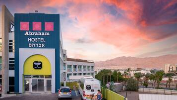 Um hostel chamado 'Abraham Hostel', com design moderno, apresentando uma entrada imponente e vista para o horizonte urbano e montanhas ao fundo.