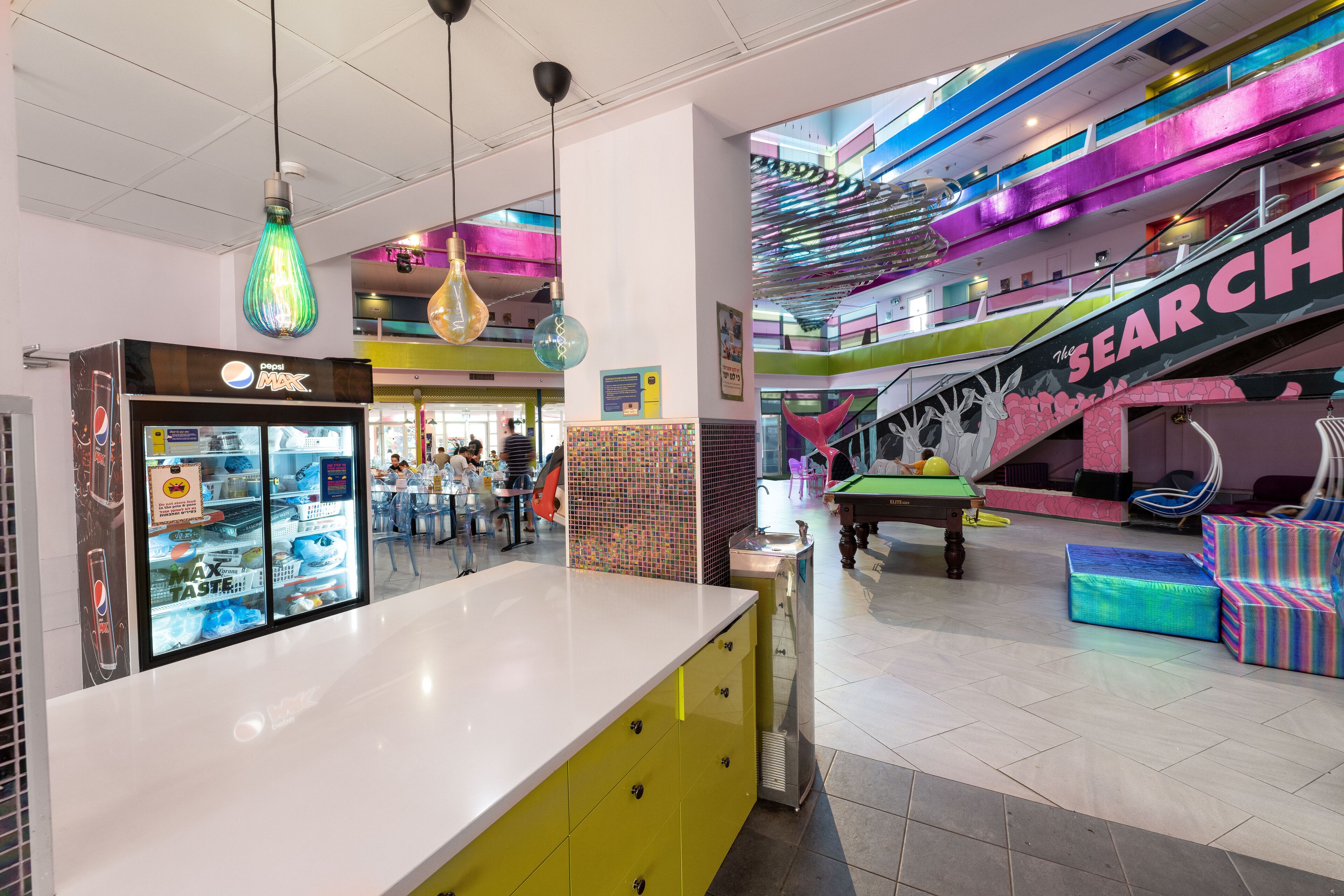 A vibrant indoor space with a colorful staircase, a vending machine, and a pool table.