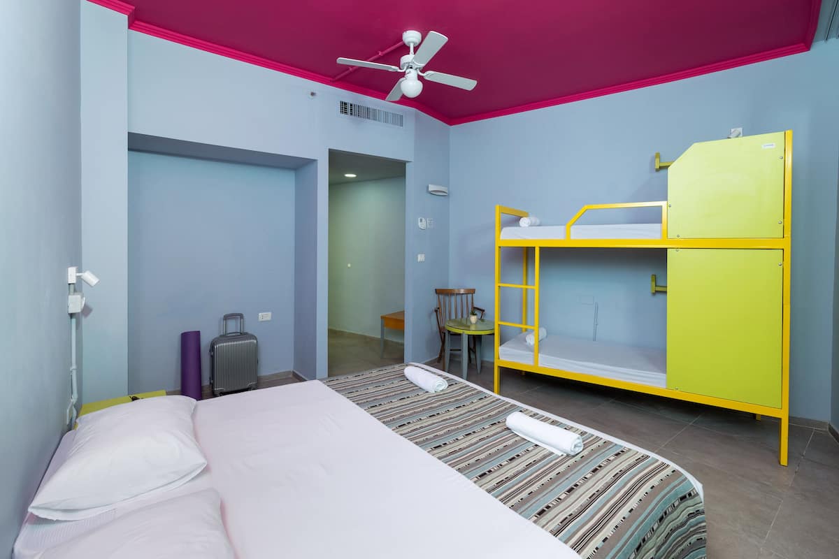 A room with a bunk bed, a single bed, a ceiling fan, a desk, and a chair.