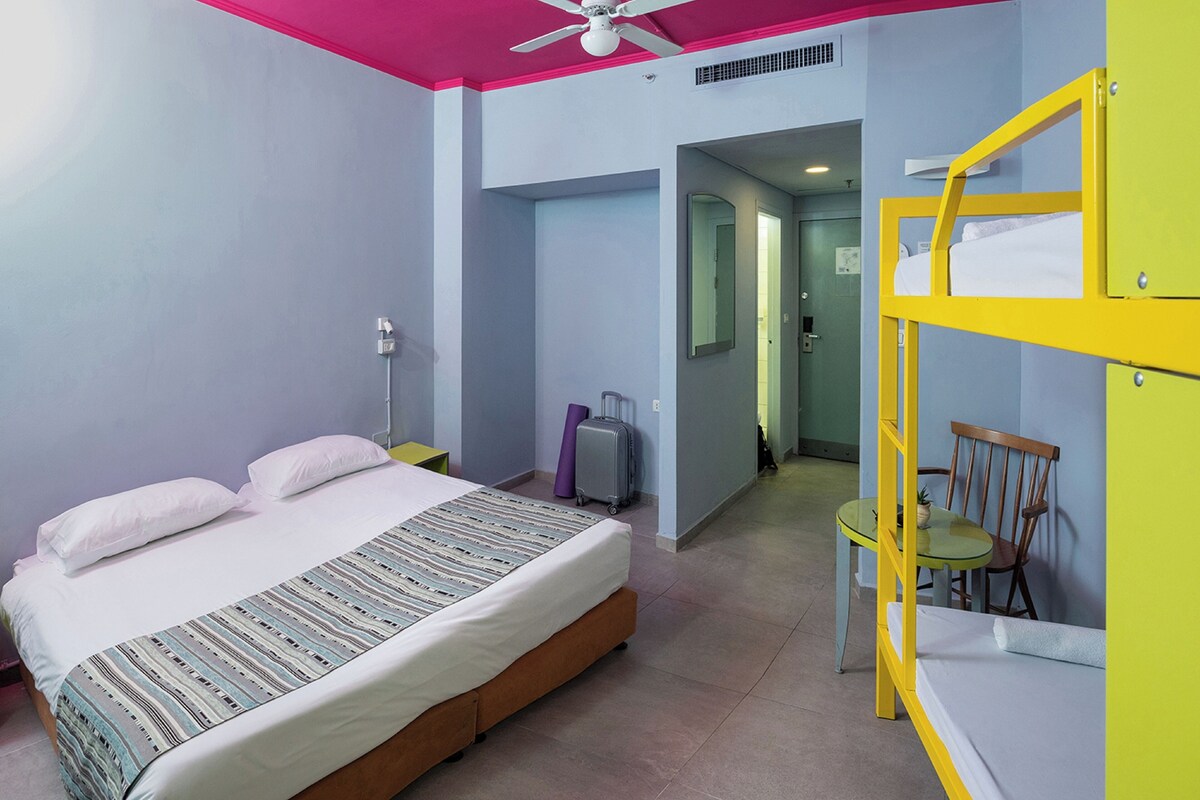 A room with a bed, a ceiling fan, a bunk bed, a suitcase, and a chair.