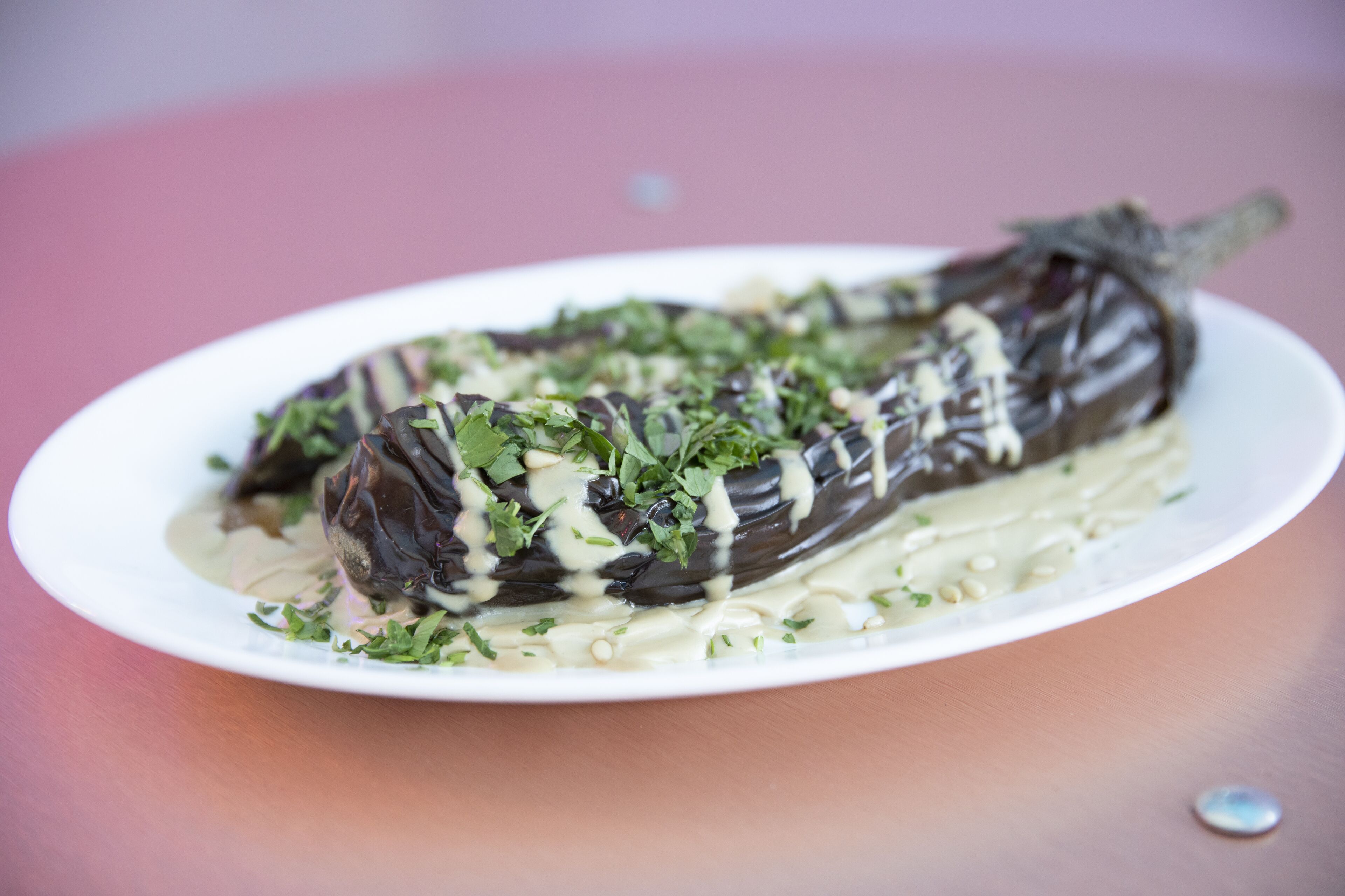 A white plate with a stuffed eggplant dish garnished with herbs and sauce.