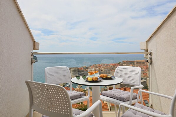 A balcony with two white chairs, a small round table, and a view of the sea and buildings. - Hedera Estate, Hedera A32 (Dubrovnik)