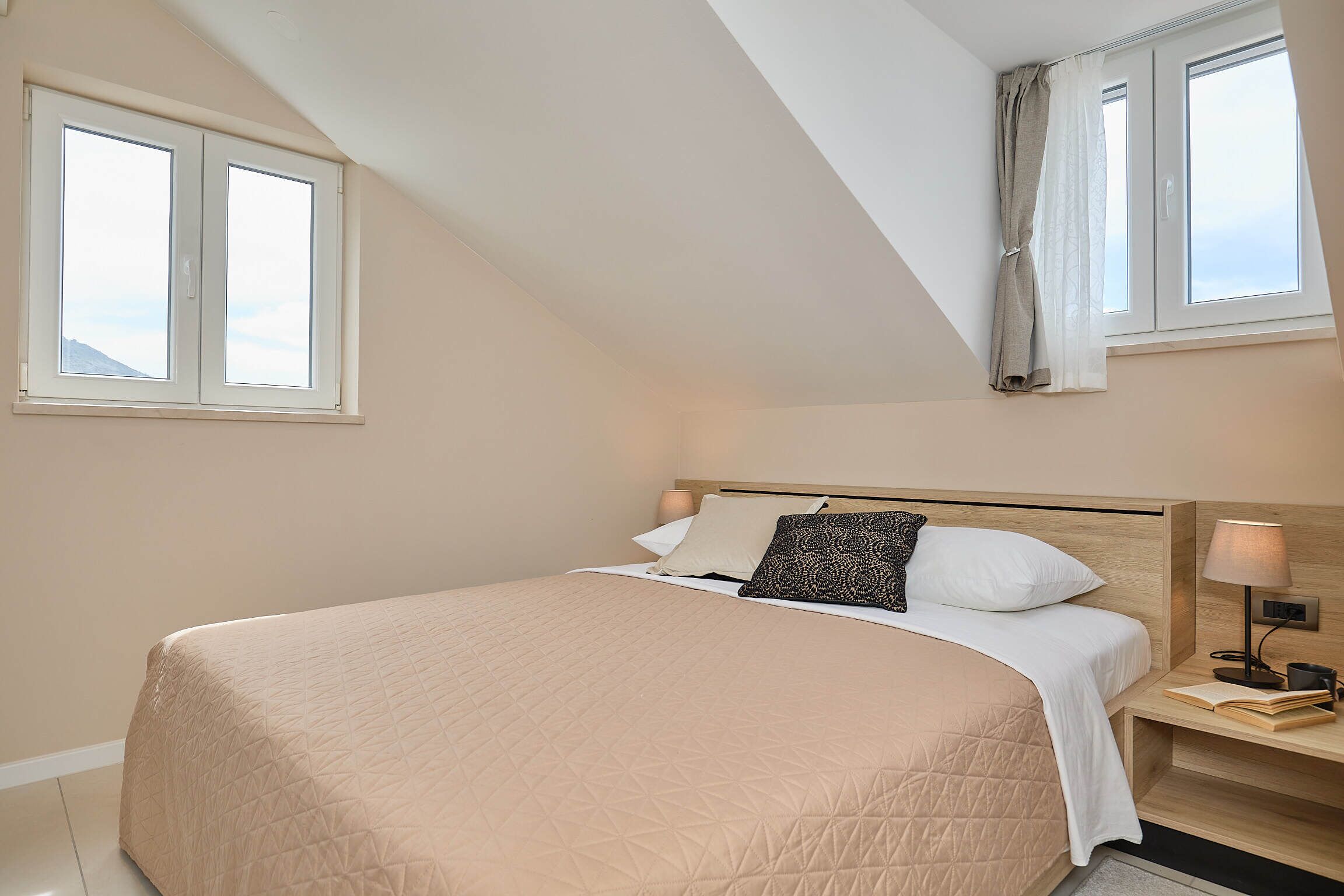 A bedroom with a bed, bedside table, lamp, and a window with curtains.