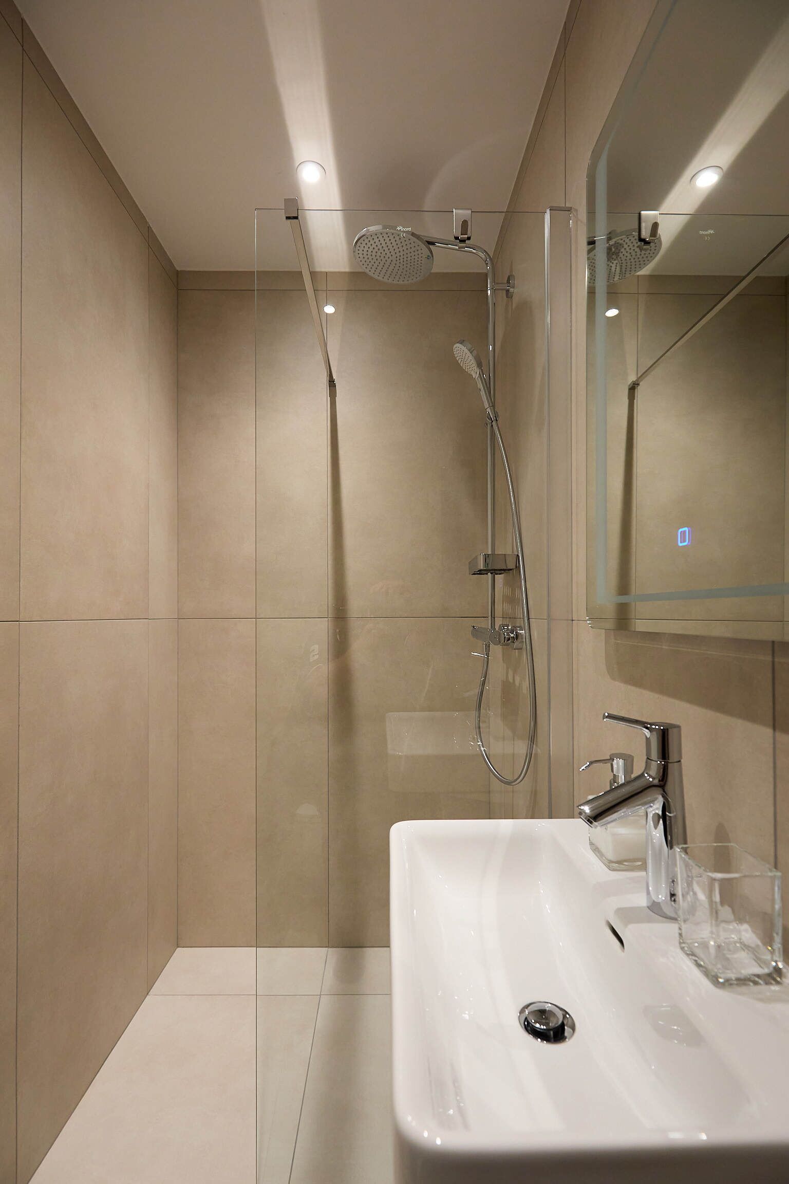 A modern bathroom with a glass-enclosed shower, a white sink, and a mirror.