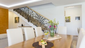 A dining area with a wooden table, white chairs, a decorative metal staircase, and artwork on the walls.