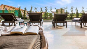 A sunlit outdoor seating area with lounge chairs and an open book, suggesting a relaxed reading spot.