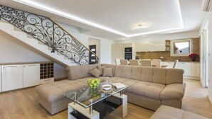 A modern living room with a glass coffee table, a beige sectional sofa, and a staircase with decorative metal railings.