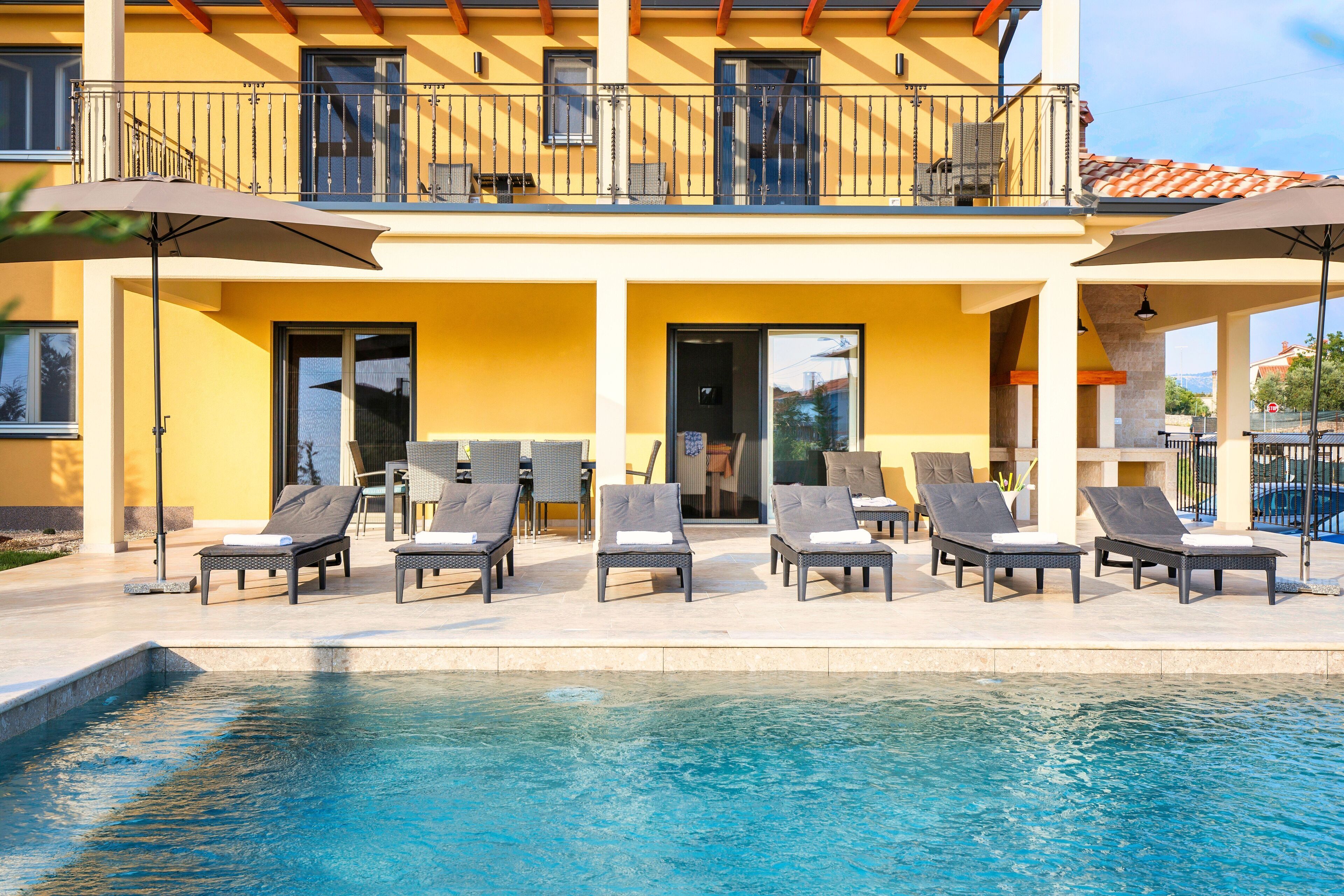A two-story building with a swimming pool, outdoor seating, and a balcony.