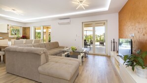 A modern living room with a sectional sofa, a glass coffee table, and a flat-screen TV. There is a sliding glass door leading to an outdoor area.